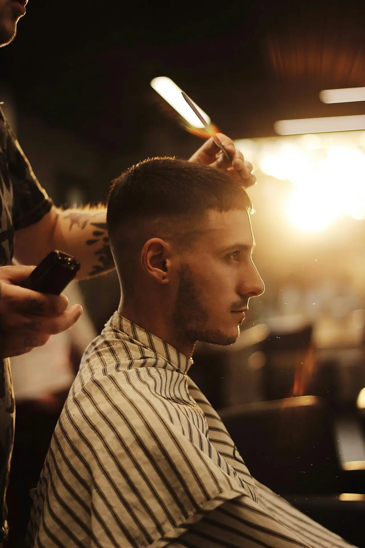 Side view of a man receiving a stylish haircut in a modern barber shop with artistic lighting.